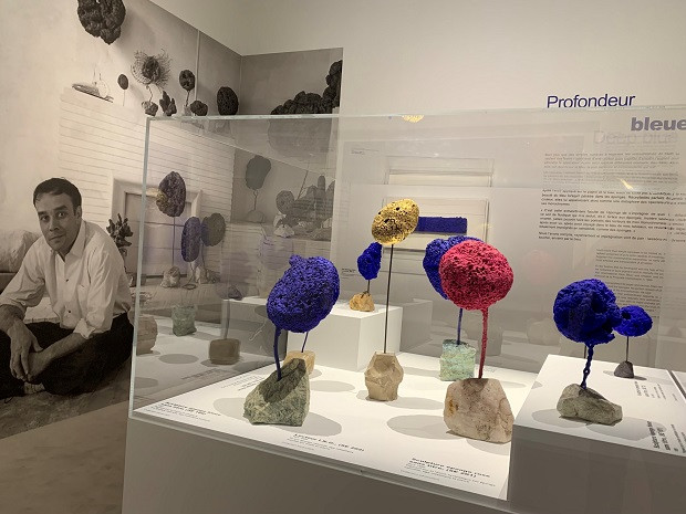 Showcase of sponge sculptures (circa 1960) in front of the portrait of Yves Klein in his apartment (1959), presented in the exhibition 
