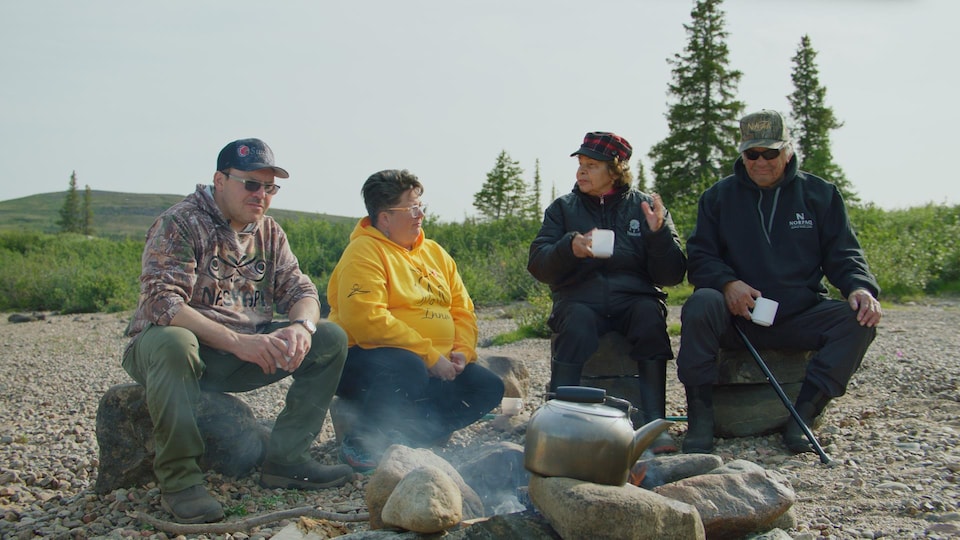 A group of people chat around the fire while drinking tea.