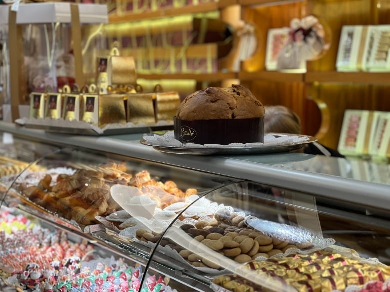 A round panettone Italian sweet bread sits on a glass display case filled with cookies, chocolates and candies.